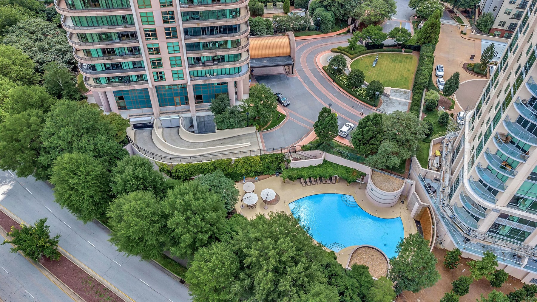 Drone view of two buildings, a swimming pool, trees and on-campus roads