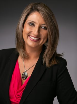 Headshot photo of a woman wearing a black blazer with a pendant